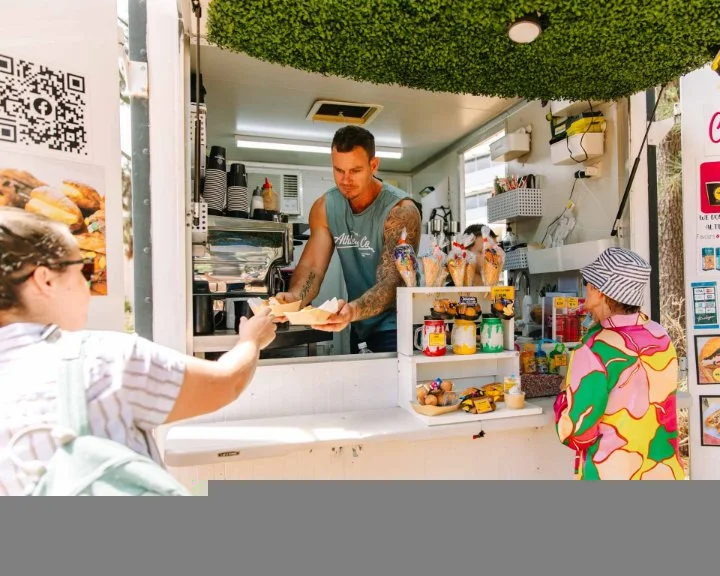 A food vendor handing takeaway food to a woman attending an event